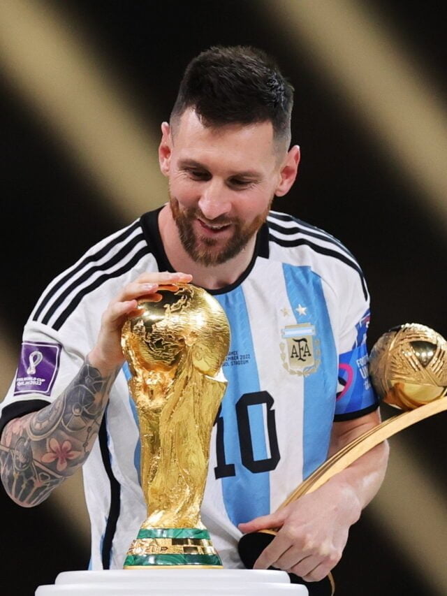 Lionel Messi posing for a photo, holding his Ballon d'Or trophy and smiling.